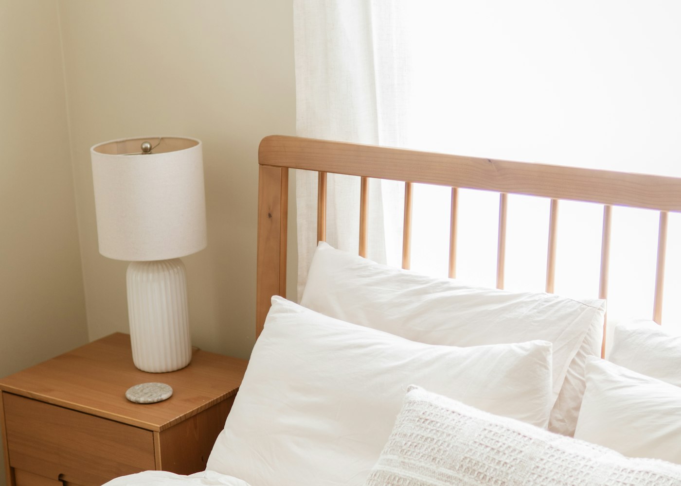 A calm, bright bedroom with white pillows, a wooden headboard and a bedside lamp