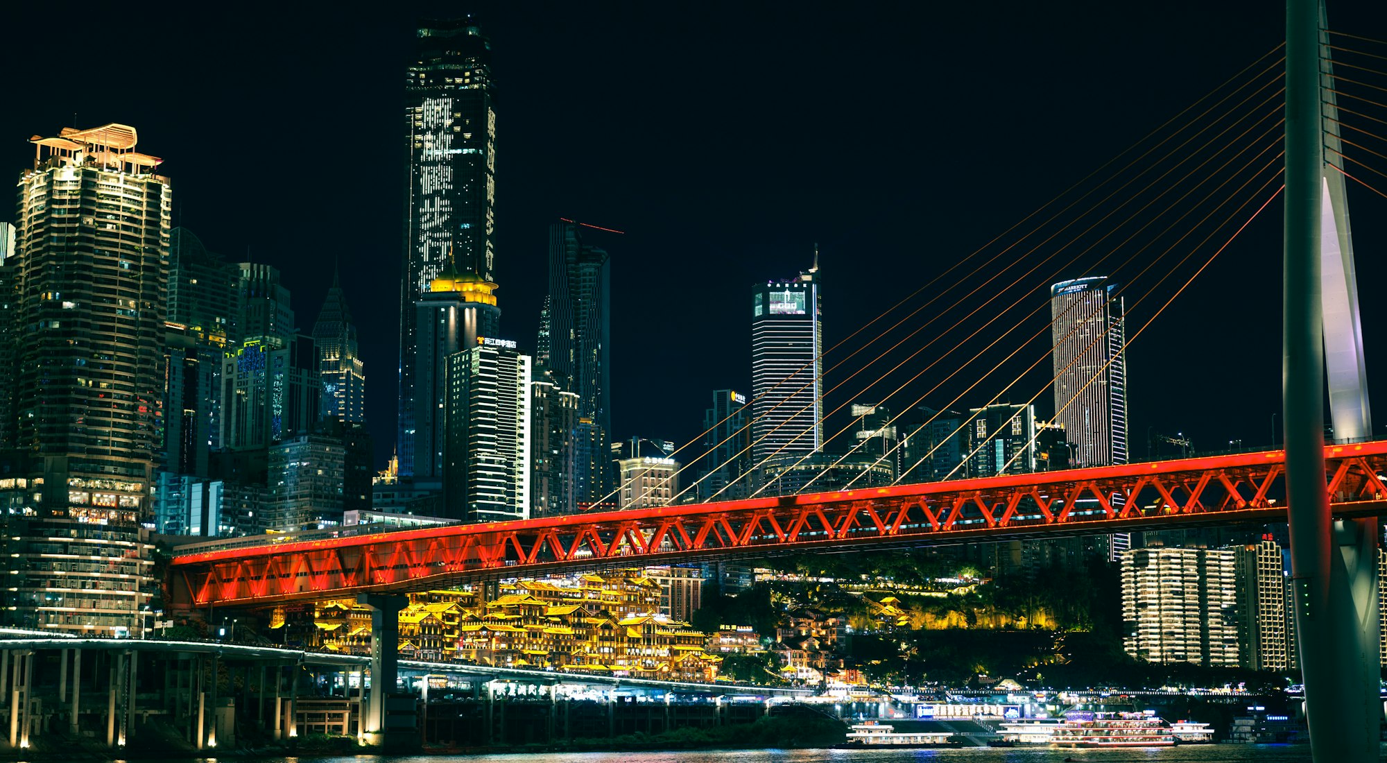 A red bridge and towers along the river at night